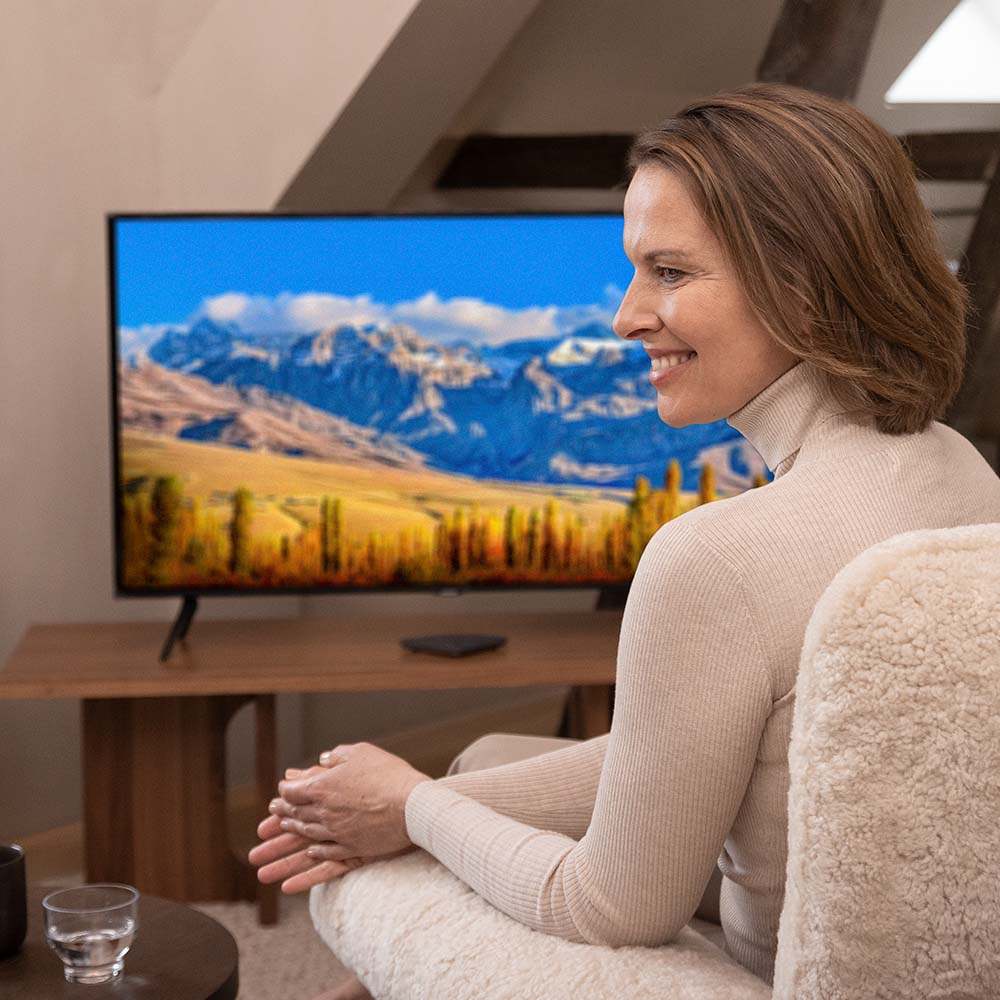 Widex TV Play 2 accessory for Allure and Moment Sheer hearing aids, showing the device connected to a TV in a living room setting.